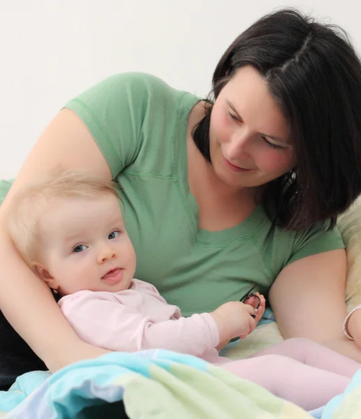 Jonge moeder met haar baby in het bed. — Stockfoto