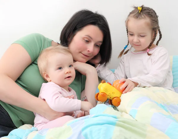 Família feliz. Jovem mãe brincando com seus filhos na cama . — Fotografia de Stock