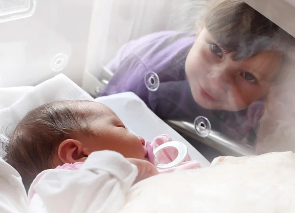 Menina recém-nascida em uma incubadora. A irmã dela a olhar . — Fotografia de Stock