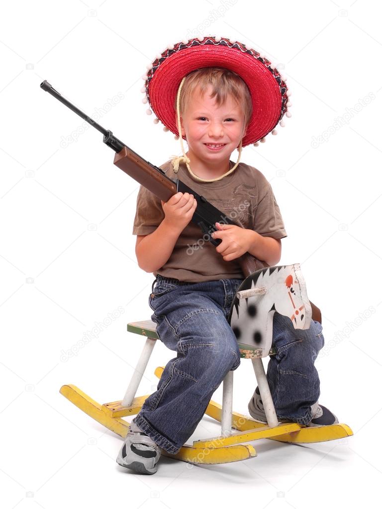 Little boy in mexican hat with gun sitting on a rocking horse.