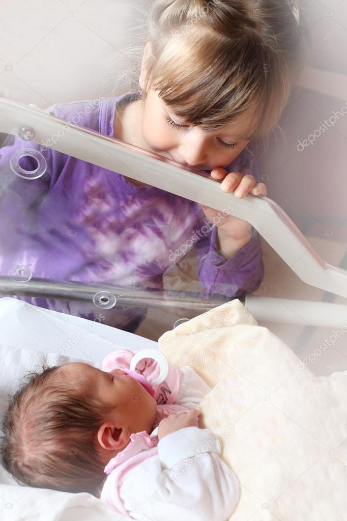 Newborn baby girl in a incubator. Her sister looking at.