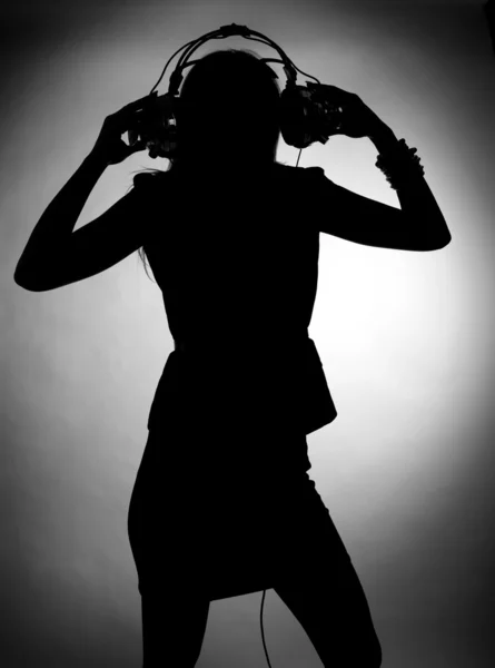 Silhouette of young woman enjoys listening music in headphones.