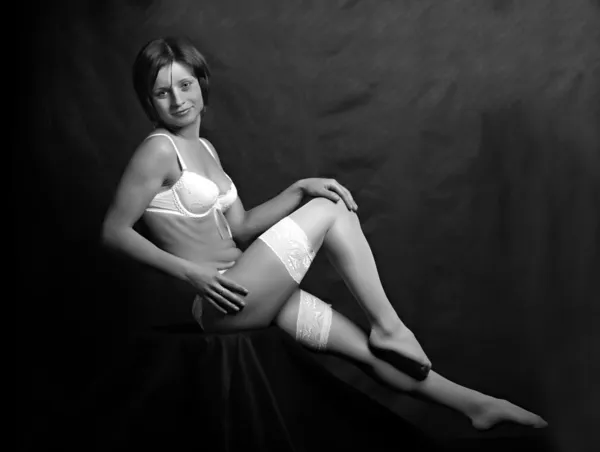 Sitting flirty girl with long slim legs in white nylons. Monochrome low key photography. — Stock Photo, Image