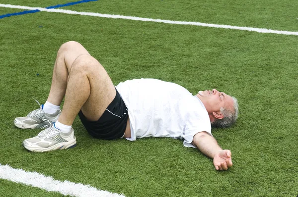 Middle age man stretching and exercising on sports field — Stock Photo, Image