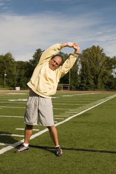 Middle age senior man stretching exercising on sports field — Stock Photo, Image