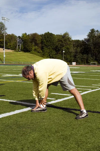 Middle age senior man stretching exercising on sports field — Stock Photo, Image