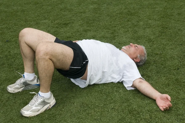 Hombre de mediana edad estiramiento y ejercicio en el campo de deportes —  Fotos de Stock