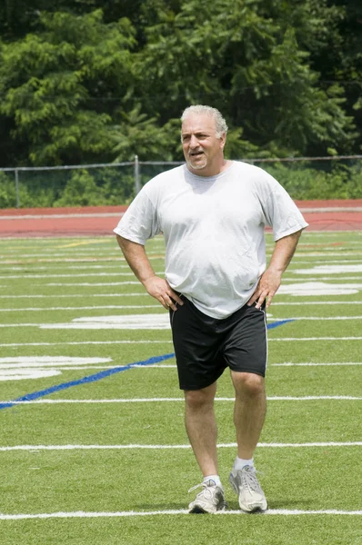 Middle age man stretching and exercising on sports field — Stock Photo, Image