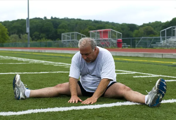 Middle age man stretching and exercising on sports field — Stock Photo, Image