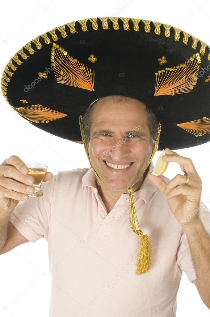 middle age senior tourist male wearing Mexican somebrero hat drinking tequila shot with slice of lemon