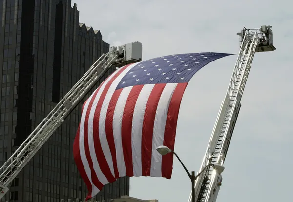 Uma grande bandeira americana pendurada entre escadas de caminhão de bombeiro Imagens De Bancos De Imagens Sem Royalties