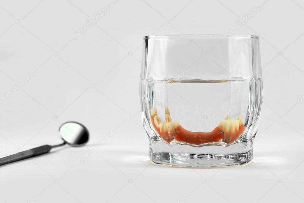 Partial denture inside glass next to dental mirror