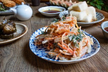 Tempura bol yağda kızartılmış sebzeler, arka planda çeşitli Japon yemekleri. Ahşap kırsal masa.