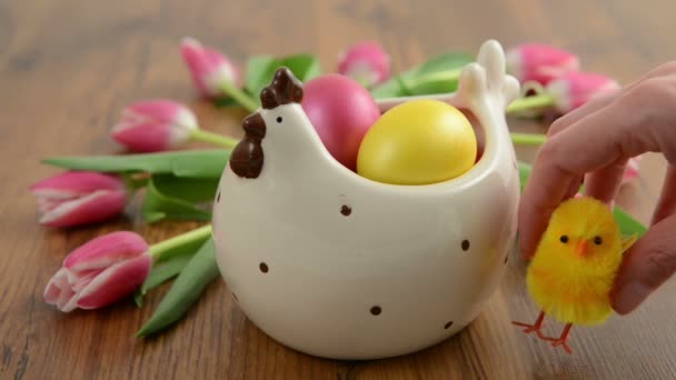 Sitting down chicken aside a chicken cup with easter eggs and tulip bunch