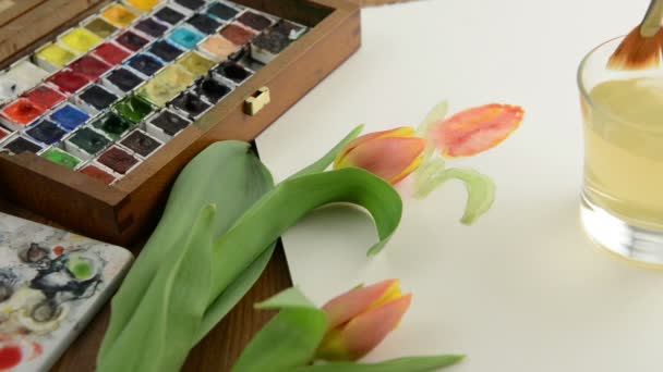 Painting with paintbrush orange tulip bud in watercolors and cleaning the brush in water glass. — Stock Video