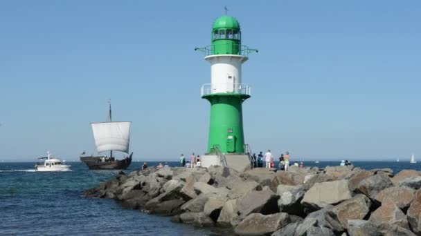 People walk to the lighthouse of Warnemünde. a cog and a motor boat ride from the Baltic Sea to the port. — Stock Video