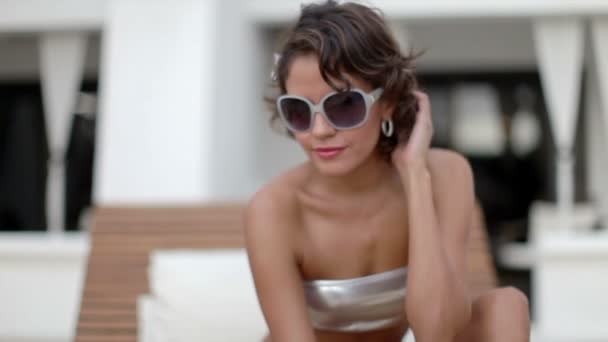 Μια σέξι γυναίκα σε ένα μπικίνι που χαλαρώνει σε μια daybed γύρω από μια πισίνα — Αρχείο Βίντεο
