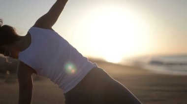genç kadın yoga bir plajda güneş doğarken uygulamaları.
