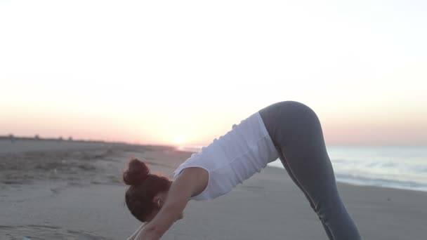 Mujer joven practica yoga en una playa al amanecer — Vídeos de Stock