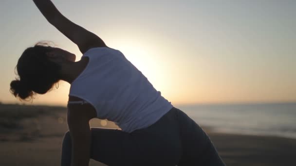 Young woman practices yoga on a beach at sunrise — Stock Video