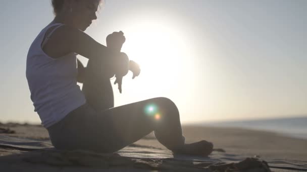 Genç kadın yoga bir plajda güneş doğarken uygulamaları. — Stok video