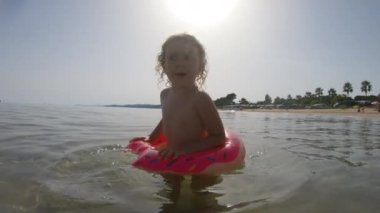 Küçük bir kız denizde şişme bir yüzükle yüzüyor.