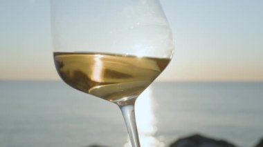 Güneş doğarken ya da batarken arkaplanda köpüklü deniz ve gökyüzü olan beyaz şarap kadehi.