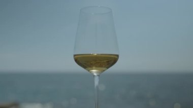 Güneş doğarken ya da batarken arkaplanda köpüklü deniz ve gökyüzü olan beyaz şarap kadehi.