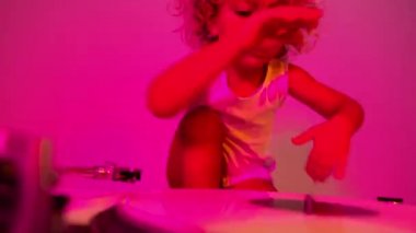 A cute djing small girl mixing vinyl on record player with coloured disco lighting