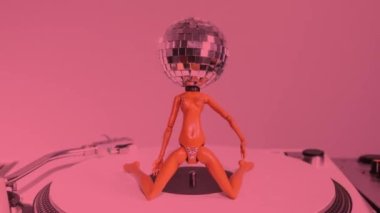 A sparkling doll with a discoball head dances on a record turntable