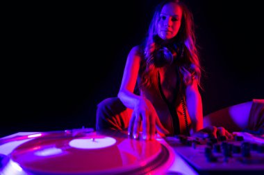 Beautiful female dj playing with turntables with blue and red contrasting lights