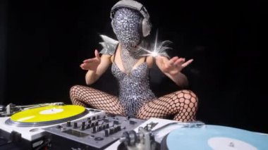Masked female dj playing with turntables in sparkling silver costume