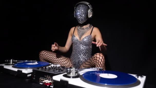 Masked female dj playing with turntables in sparkling silver costume