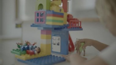 Cute blonde haired child sitting at table and playing with building blocks