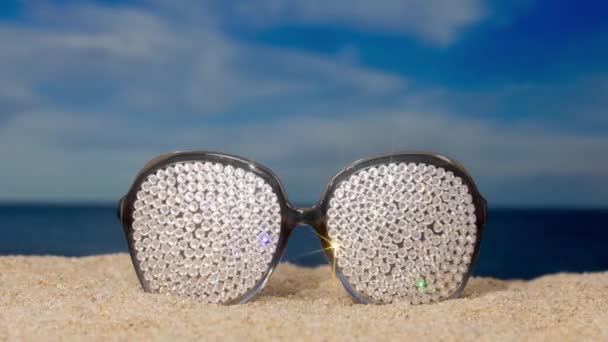 海滩上有一副闪烁着太阳镜的水晶 上面点缀着过往的云彩 — 图库视频影像