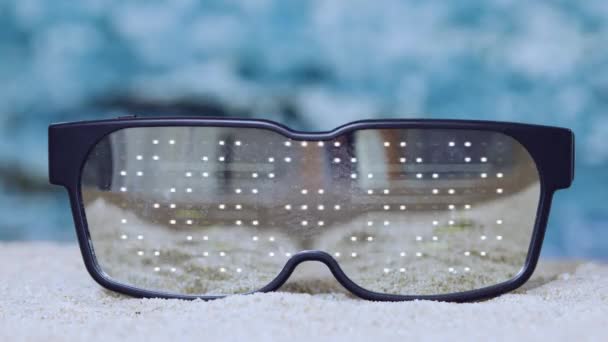海滩上有一副带着未来色彩的太阳镜 上面闪烁着大海的光芒 — 图库视频影像