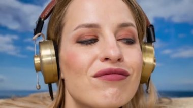 Kafasına kadar plaja gömülü güzel bir kadın kulaklıkla müzik dinliyor.
