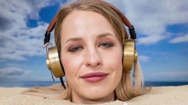 Kafasına kadar plaja gömülü güzel bir kadın kulaklıkla müzik dinliyor.