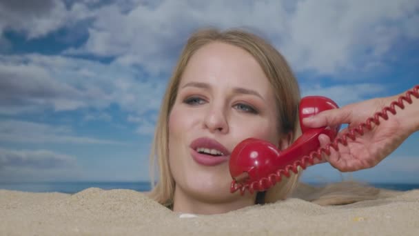 一个漂亮的女人把头埋在海滩上 用红色的老式电话交谈 — 图库视频影像