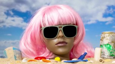 Plaj çöplük ve çöplerle dolup taşarken kuma sıkışmış plastik bir kadın manken kafası.