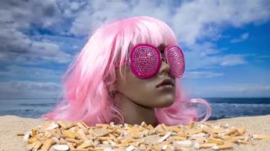 Plajda sigara izmaritleri biriken plastik bir kadın manken kafası.