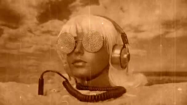 ビーチに輝くサングラスとヘッドフォンで砂の中に立ち往生プラスチック女性マネキンの頭 — ストック動画