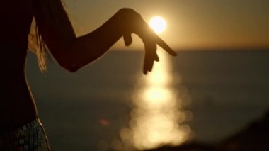 Gün doğumunda parıldayan bir deniz ve gökyüzüne karşı ritmik bir şekilde hareket eden kadın kolları. 