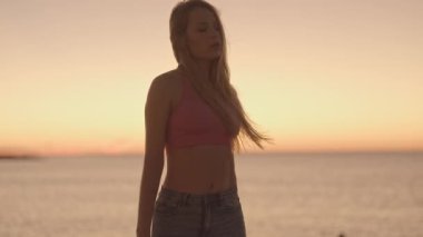 Güneşin doğuşunda ışıl ışıl bir deniz ve gökyüzüne karşı güzel bir kadın.