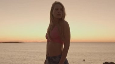 Güneş doğarken ışıldayan bir deniz ve gökyüzüne poz veren güzel bir kadın.