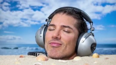 Sahilde boğazına kadar gömülü bir adam kulaklıkla müzik dinliyor.