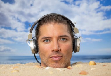 Sahilde boğazına kadar gömülü bir adam kulaklıkla müzik dinliyor.
