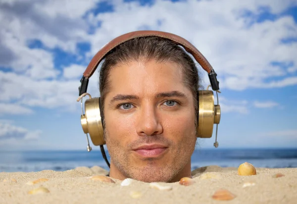 ヘッドフォンで音楽を聴くビーチで頭の上に埋められた男 — ストック写真