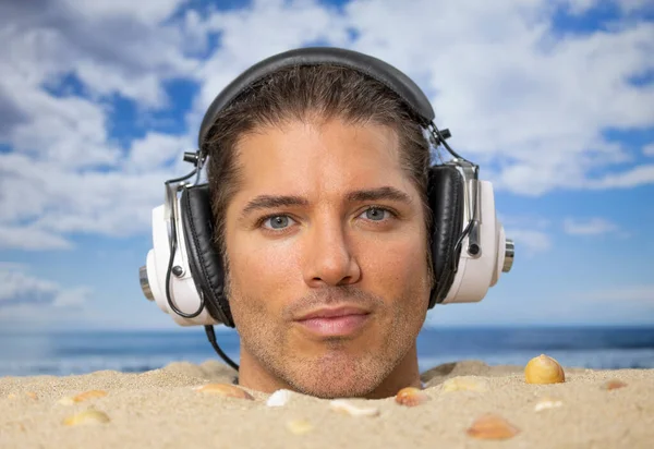 ヘッドフォンで音楽を聴くビーチで頭の上に埋められた男 — ストック写真