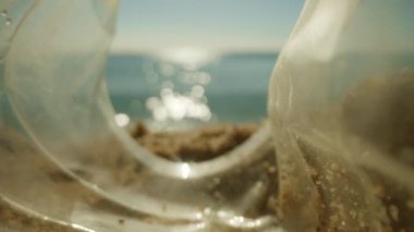 Çöp ve çöplerle dolu güneşli güzel bir sahil. Plastik bir şişenin içinden görünen deniz